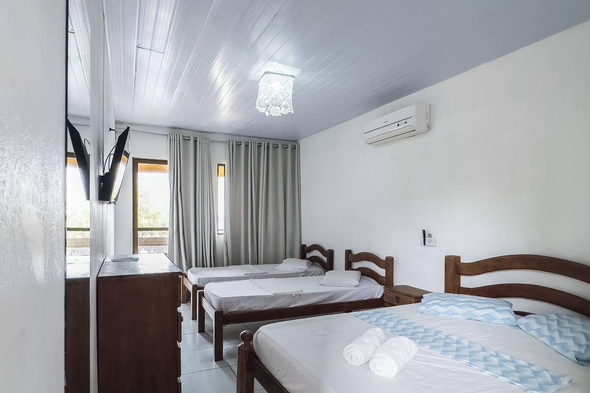 A hotel room with two single beds, a wooden dresser, a ceiling fan, and an air conditioning unit.