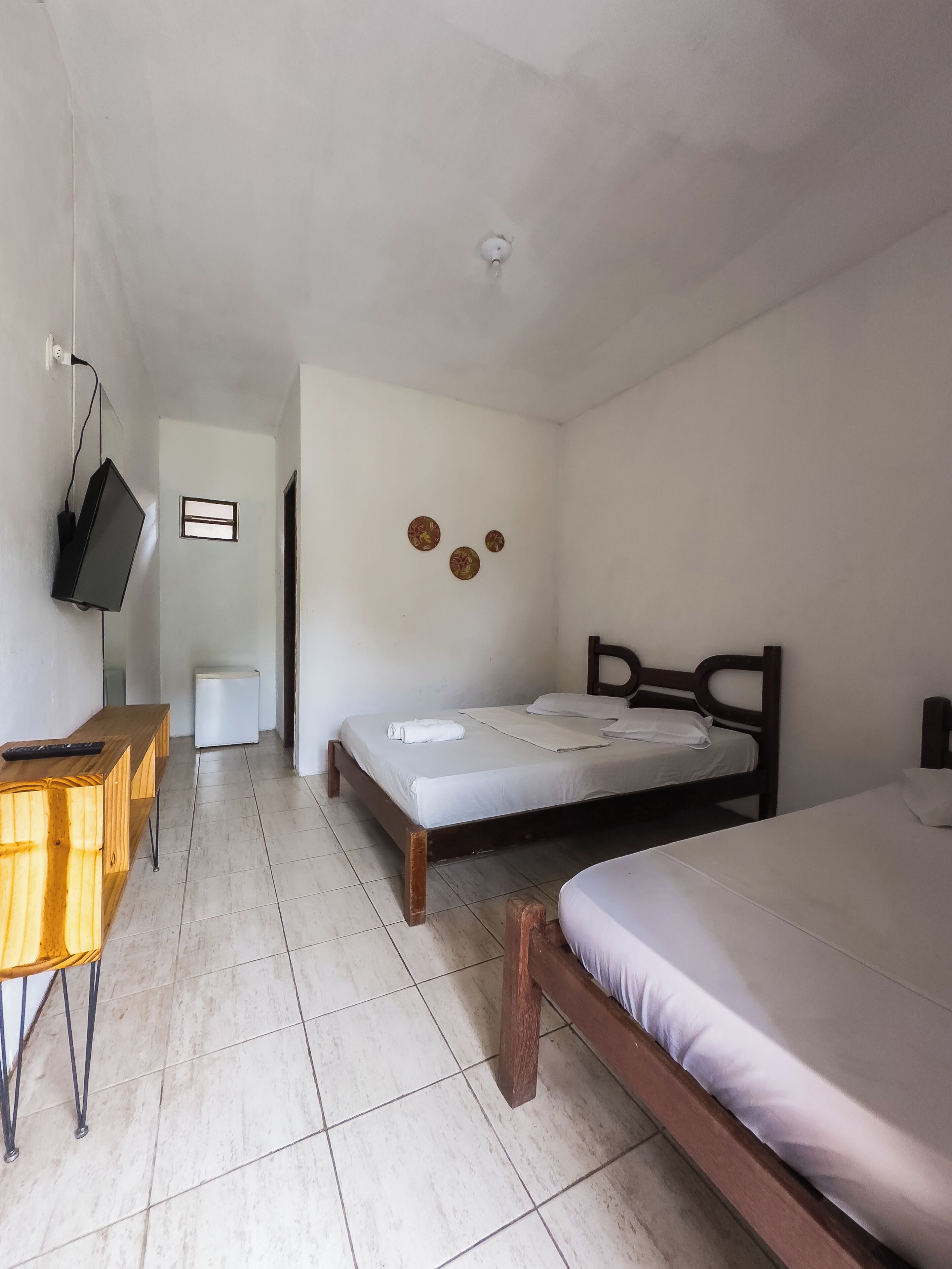 Un dormitorio con dos camas, un escritorio de madera, un televisor montado en la pared y una ventana pequeña.