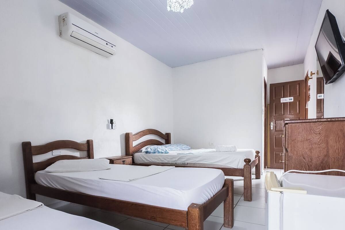 A room with two wooden beds, a white refrigerator, and a television mounted on the wall.