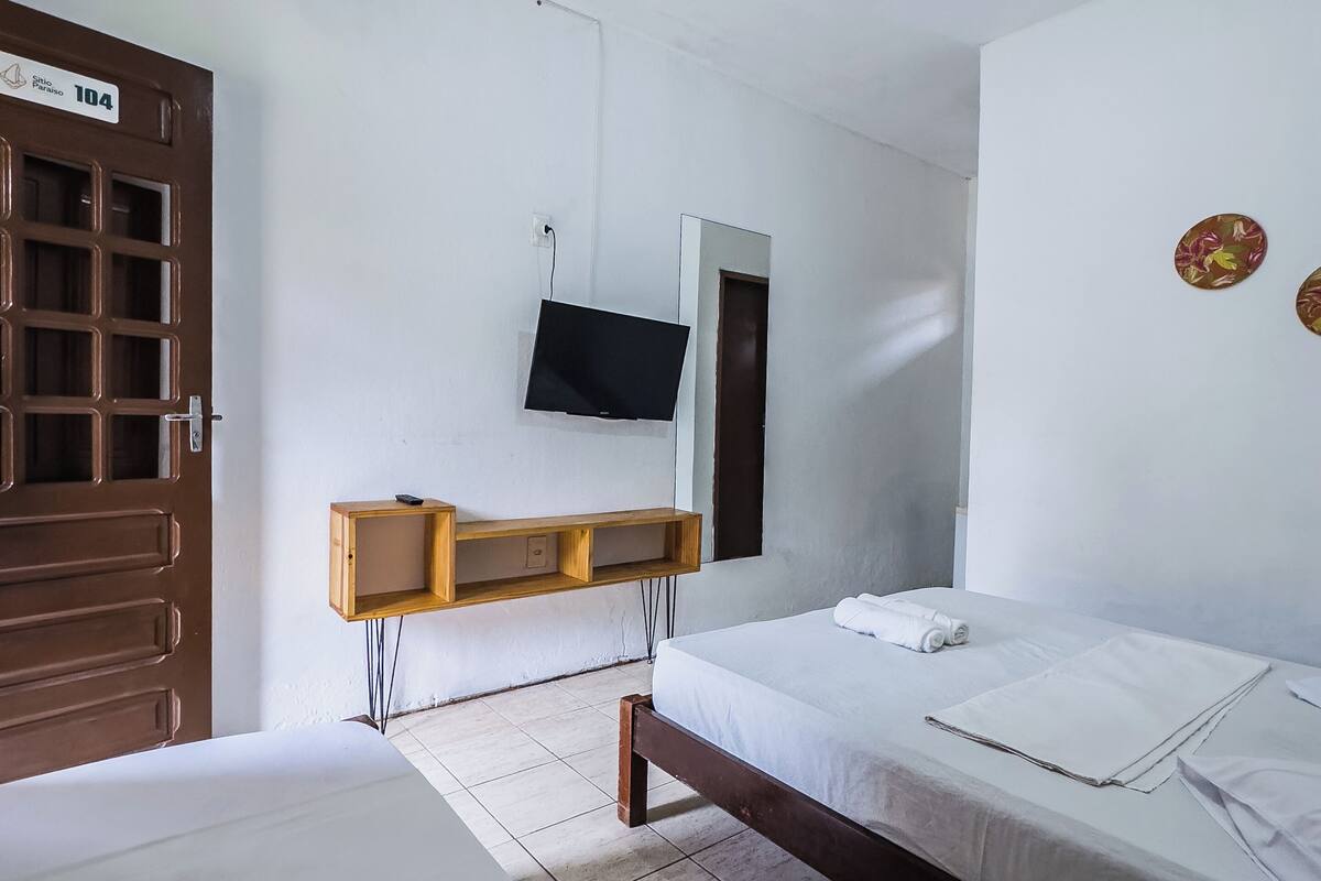 A room with two beds, a TV mounted on the wall, a wooden shelf, and a door with a number sign.