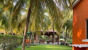 A well-maintained garden with palm trees, a brick gazebo, and a grassy lawn.