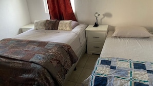 A room with two beds, a nightstand with a lamp, and a window with red curtains.