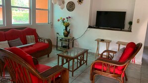 A living room with a red sofa, two wicker chairs, a coffee table, and a TV mounted on the wall.