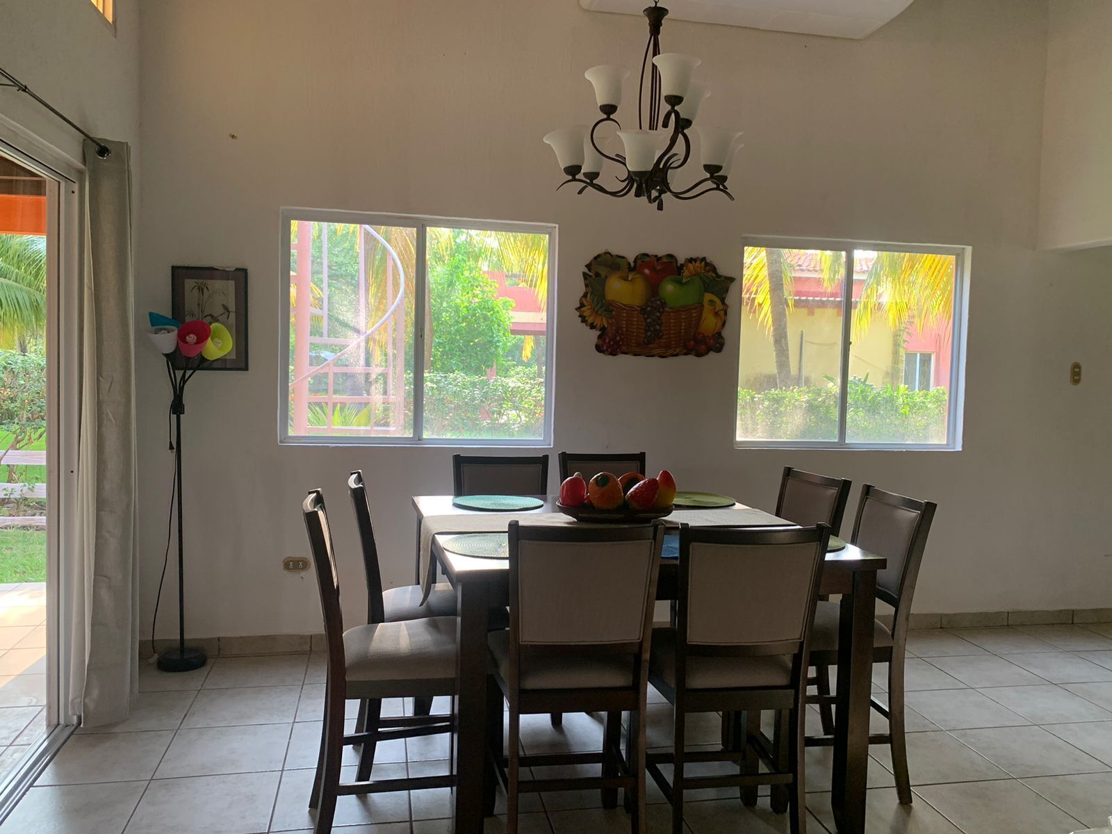 A dining area with a table set for four, surrounded by chairs, a chandelier, and a fruit basket on the wall.