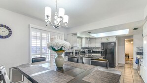 A modern kitchen with a central island, a dining area with a large table and chairs, and a chandelier. - Havasu War Eagle - Pool, Games, Serene Stay (Lake Havasu City)