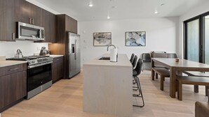 Een moderne keuken met donker houten kastjes, roestvrijstalen apparatuur en een centraal eiland met barstoelen.