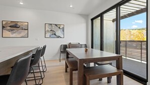 Een moderne eetruimte met een lange tafel, meerdere stoelen en twee abstracte schilderijen aan de muur.