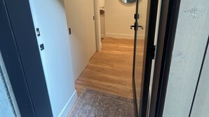 Un pasillo con suelo de madera, un recibidor con alfombra, una puerta y un espejo en la pared.