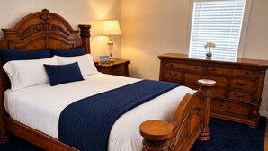 Una cama bien hecha con cabecera de madera, una mesita de noche con lámpara, un aparador y una ventana con persianas.