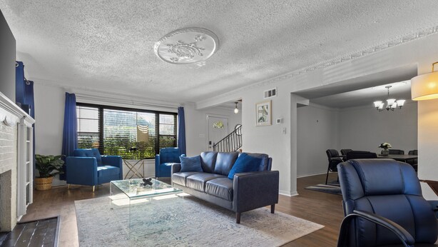 Una sala de estar moderna con chimenea, sofás azules, una mesa de centro de vidrio y un comedor al fondo.