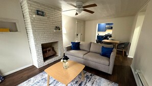 Una sala de estar con chimenea, un sofá, una mesa de centro y una cocina al fondo.