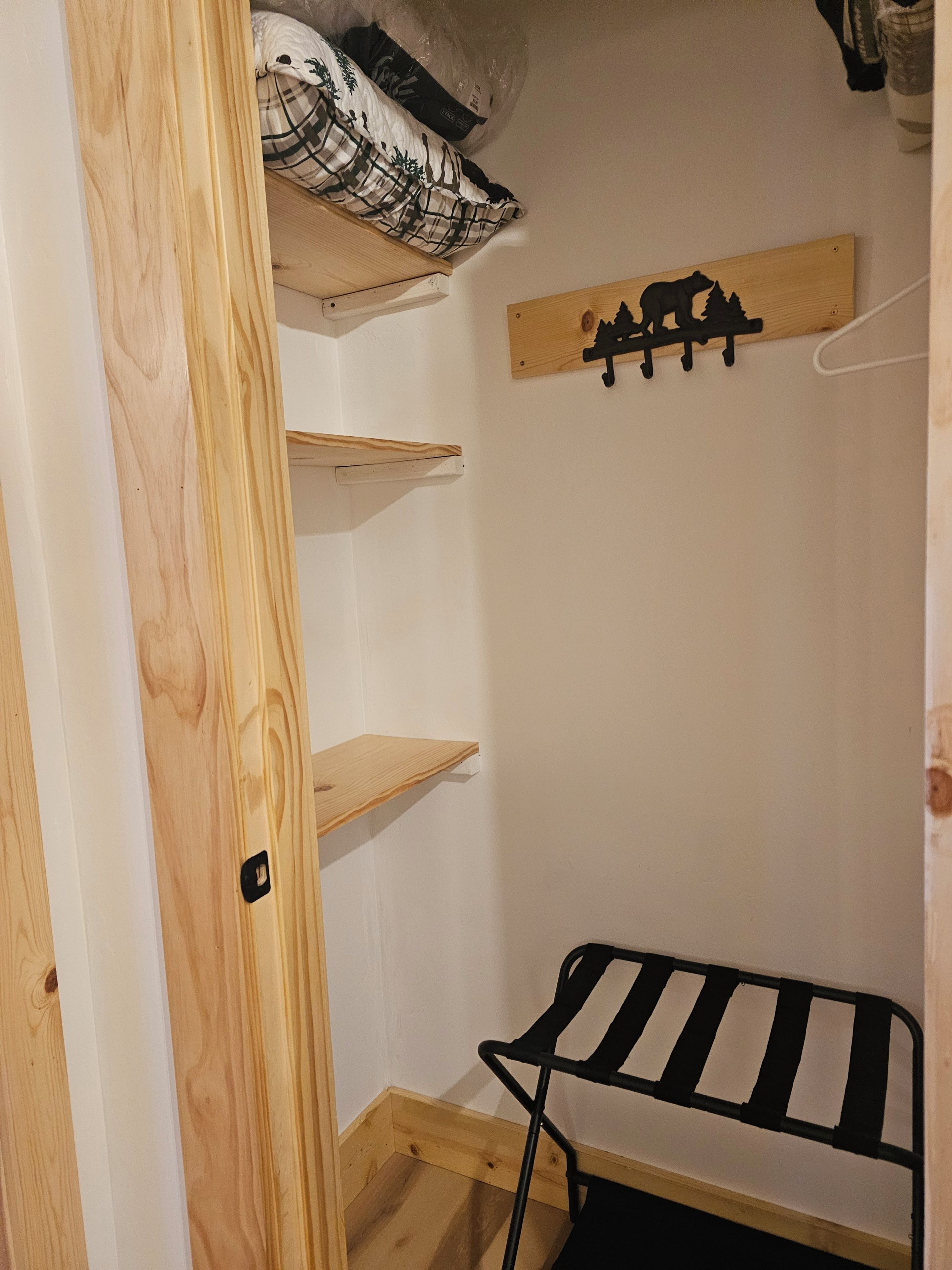 A small, compact room with a wooden wardrobe, a bed with a black and white striped mattress, and a wall-mounted coat rack.