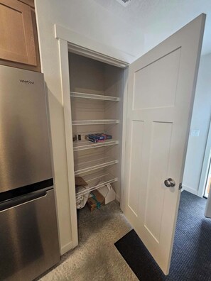 A kitchen with a stainless steel Whirlpool refrigerator, white shelving, and a closed white door. - Cozy 2BR Home Parking and Full Kitchen (Stanfield)