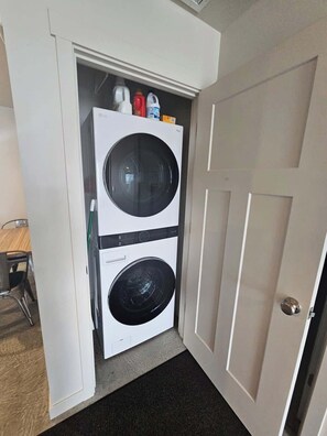 Un lavadero con lavadora y secadora de carga frontal, una mesa pequeña con sillas, y una puerta que da a otra habitación.