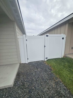 A gated outdoor area with a gravel path leading to a building entrance. - Cozy 2BR Home Parking and Full Kitchen (Stanfield)