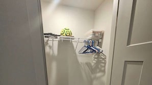 Une petite pièce étroite, dotée d’une étagère intégrée, d’une poubelle verte et d’un porte-vêtements suspendu.