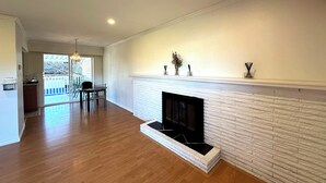 Uma sala de estar ampla com lareira, piso de madeira, área de jantar com mesa e cadeiras, e vista para o deck externo.