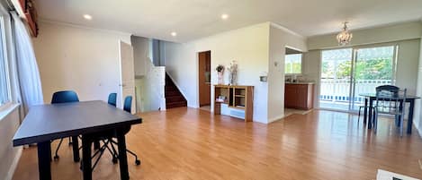 A spacious living area with a dining table, chairs, a staircase, and a kitchen area.