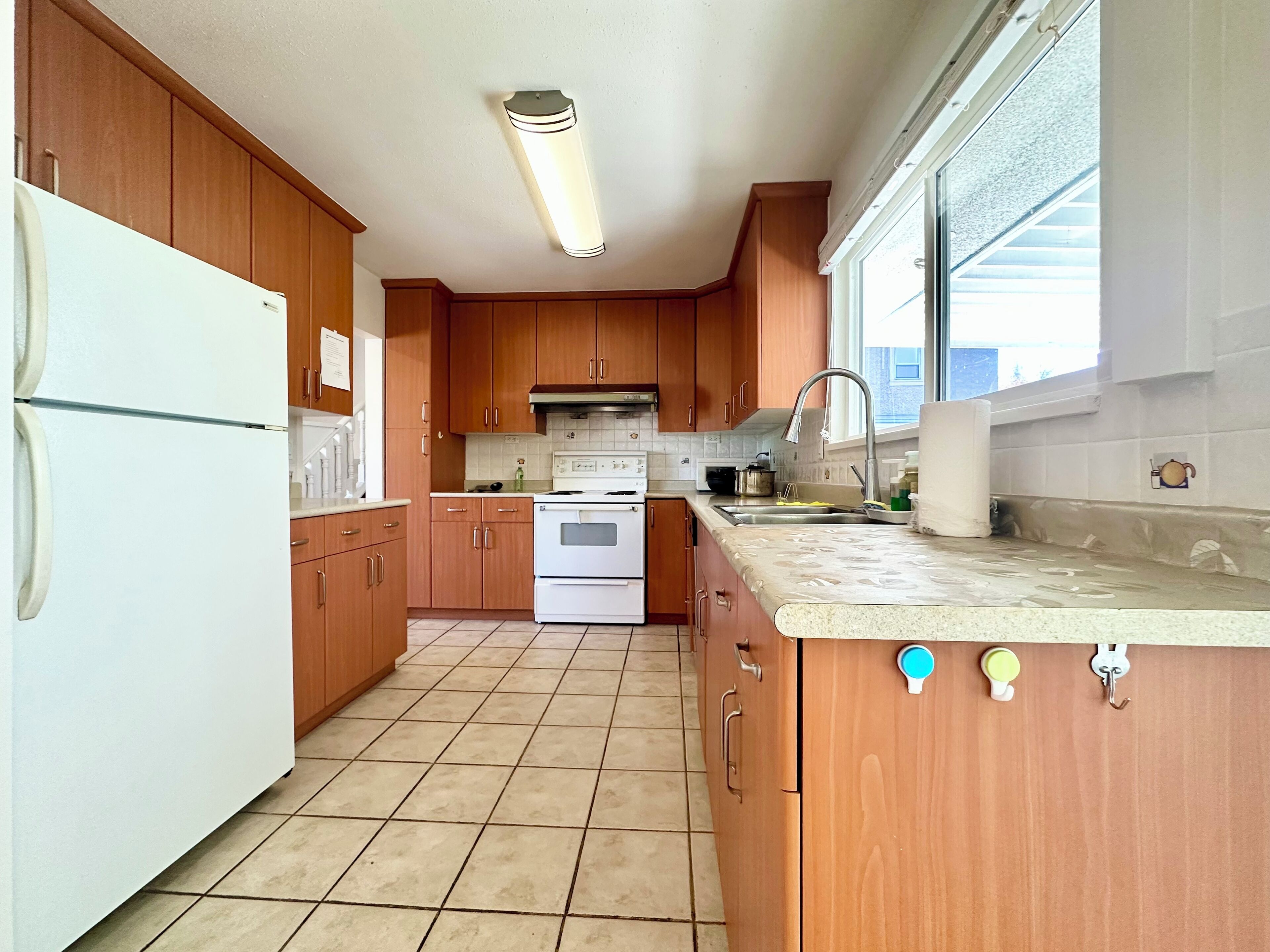 Une cuisine avec des meubles de rangement en bois, un réfrigérateur blanc, une cuisinière et une fenêtre qui laisse entrer la lumière naturelle.