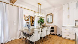 A dining area with a wooden table, white upholstered chairs, a chandelier, and white cabinetry. - Lakefront Home with Pool and Hot tub (Cornelius)