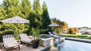A poolside area with lounge chairs and umbrellas, surrounded by greenery and a view of a residential area. - Lakefront Home with Pool and Hot tub (Cornelius)