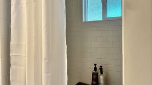 A bathroom with white tiled walls, a window, a wooden bench, and two bottles of hair care products. - Cozy 1-Bedroom Guesthouse in the Country with HVAC, in Lodi (Lodi)