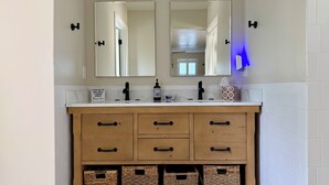 A bathroom with a double vanity, two mirrors, a light fixture, a soap dispenser, and wicker baskets under the vanity. - Cozy 1-Bedroom Guesthouse in the Country with HVAC, in Lodi (Lodi)