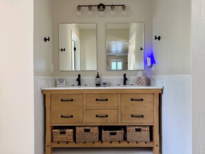 Un bagno con doppio lavabo, due specchi, un lampadario, un erogatore di sapone e cesti in vimini sotto il lavabo.