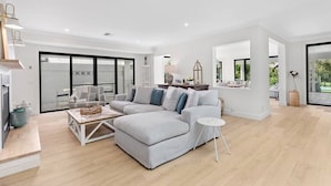 A spacious living room with a large grey sectional sofa, a coffee table, and a small side table. There is a sliding glass door leading to a balcony with a view of greenery. - Whitepepper Cottage, Pokolbin, Hunter Valley (Pokolbin)