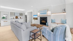 A modern living room with a fireplace, a grey sofa, a striped sofa, and a wooden coffee table. - Whitepepper Cottage, Pokolbin, Hunter Valley (Pokolbin)
