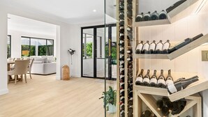 A modern interior with a wine rack, a dining area, and a glass door leading to an outdoor space. - Whitepepper Cottage, Pokolbin, Hunter Valley (Pokolbin)