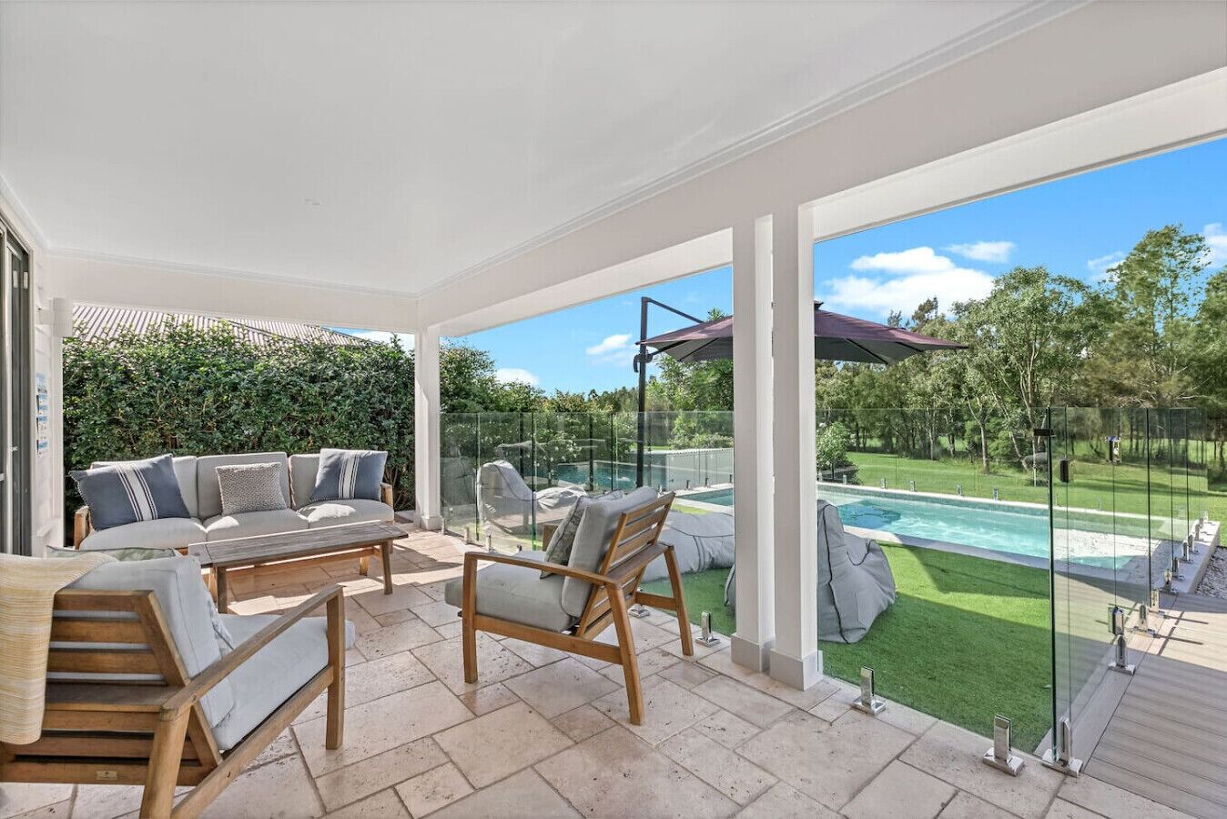 A covered outdoor seating area with a pool and lawn in the background.