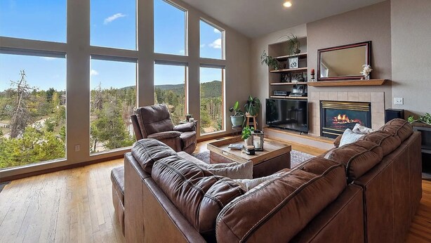 A spacious living room with large windows, a fireplace, leather sofas, and a television. - Luxury Evergreen Retreat · Fireplace · Mountain Views · 45 min Denver  (Evergreen)