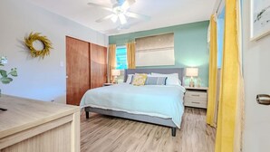 A bedroom with a bed, bedside tables, a ceiling fan, a wooden wardrobe, and a wall-mounted mirror. - 3 BDRM Florida Charmer in Venice FL- Private Pool+King Bed+Parking for Boats/RVs (Venice)