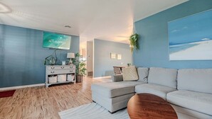A modern living room with a grey sofa, a wooden coffee table, and a flat-screen TV mounted on the wall. - 3 BDRM Florida Charmer in Venice FL- Private Pool+King Bed+Parking for Boats/RVs (Venice)