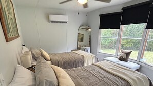 Une chambre avec deux lits, un ventilateur de plafond, une fenêtre donnant sur un espace verdoyant et un miroir au mur.