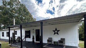 Un bâtiment blanc orné d’une étoile noire sur le mur, un porche avec des chaises et une bordure en pierre.