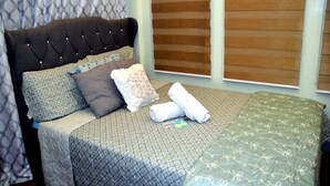 A neatly made bed with patterned bedding, a headboard with buttons, and a window with blinds.