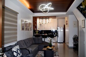 A modern living room with a grey sectional sofa, a coffee table with a vase, and a kitchen area in the background.