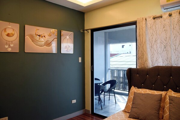 A bedroom with a bed, a balcony with chairs, and artwork on the wall.