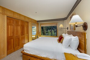 A hotel room with a large bed, wooden wardrobe, a window with a view of trees, and a wall-mounted lamp. - Ski-in/Ski-out, Big Sky Resort, Community Pool/Hot Tub! (Big Sky)