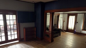 Ett rymligt vardagsrum med trägolv, en platt-TV som är monterad på väggen, en mörk lädersoffa och ett soffbord med fjärrkontroller.