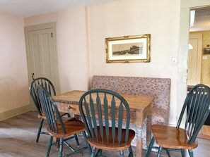 A dining area with a wooden table, four chairs, a bench, and a framed picture on the wall.