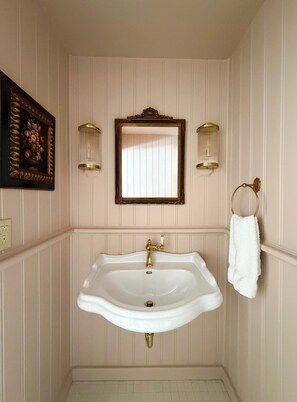 Une salle de bain avec un lavabo blanc, un miroir et deux appliques murales.