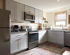 A modern kitchen with built-in appliances, a large window, and a patterned rug. - Historic Ski House, Walk to Town, Short Drive to Slopes (Jamaica)