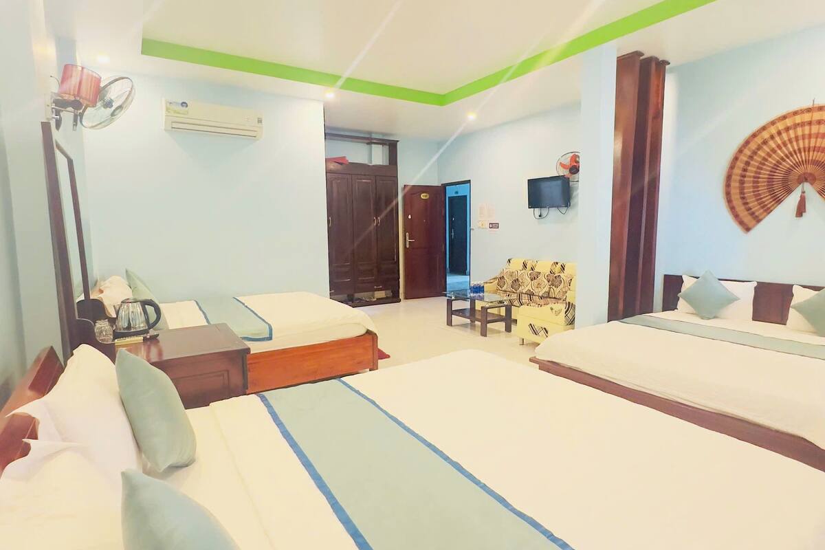 A hotel room with two beds, a desk, a chair, an air conditioning unit, and a television.