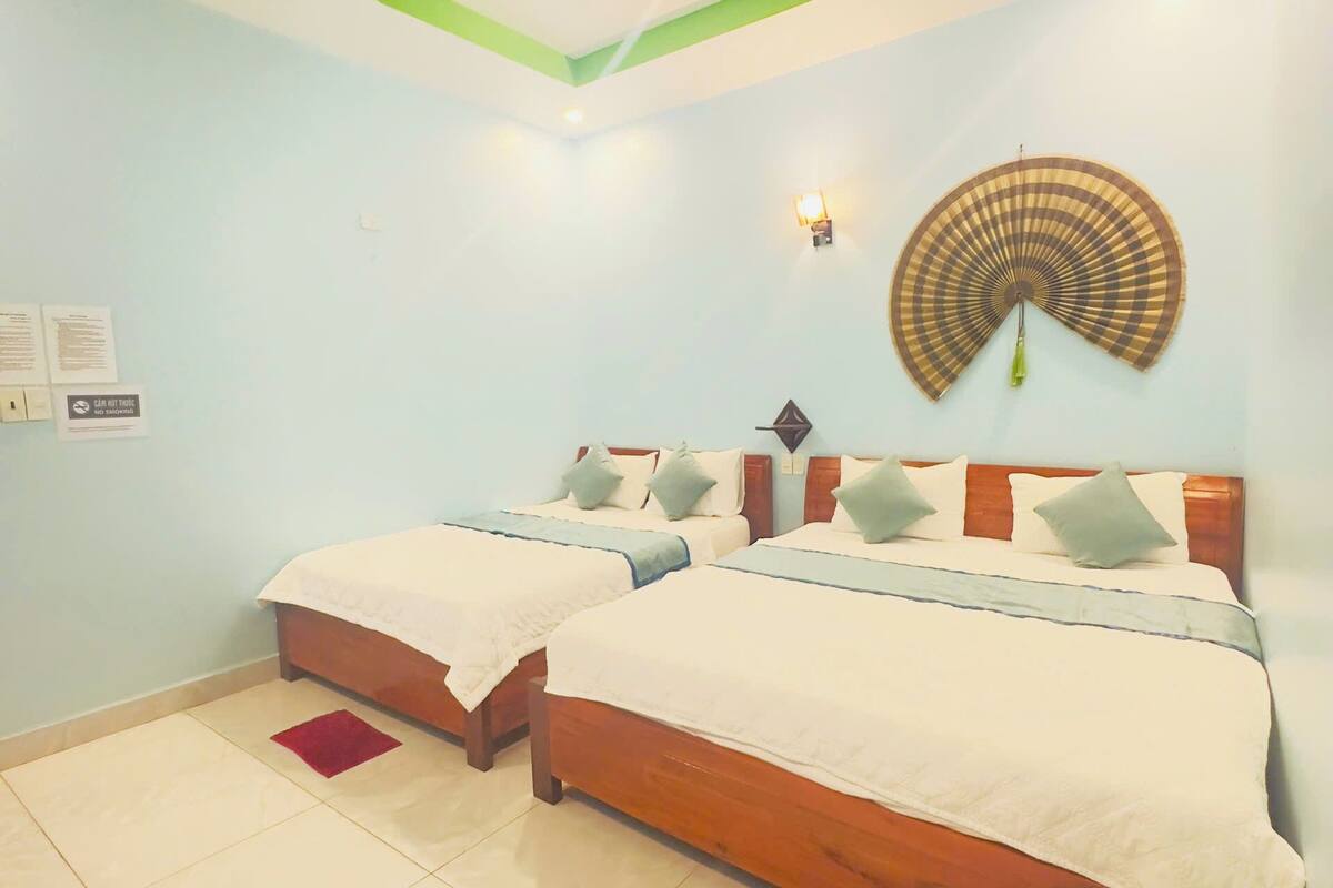 A hotel room with two wooden beds, a green accent on the ceiling, a wall-mounted fan, and a red rug.