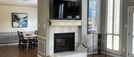 A spacious living room with a fireplace, a dining area, and a large window.