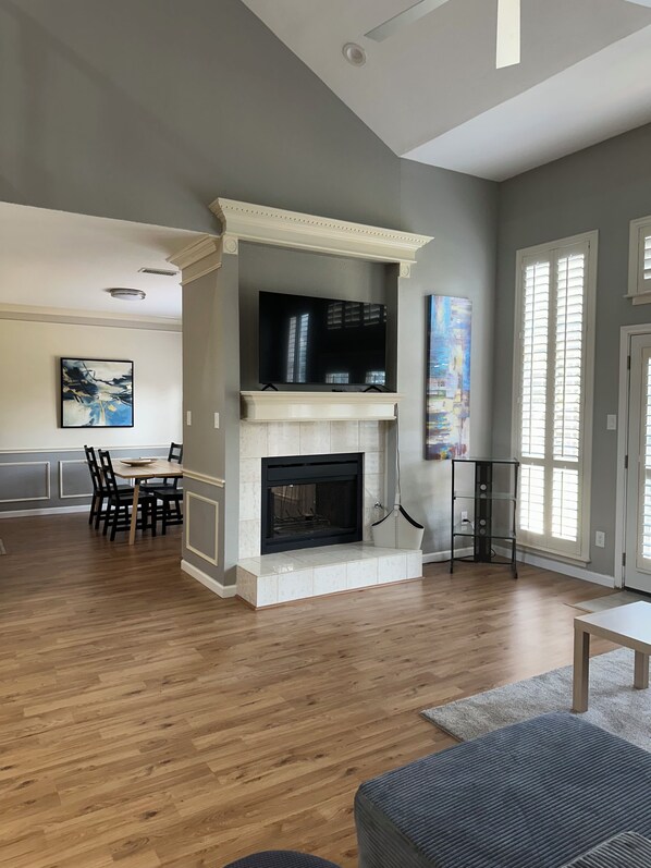 A spacious living room with a fireplace, a dining area, and a large window.
