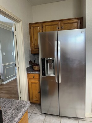 A stainless steel refrigerator with a water dispenser, wooden cabinets, and a granite countertop in a kitchen.